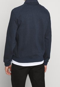 Sweat-shirt bleu marine avec col à revers, poignets et taille côtelés. Confectionné dans un tissu doux à la texture lisse. Design simple, sans motifs.