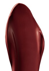 Głęboka czerwona pomadka do ust o gładkiej fakturze, prezentująca błyszczące wykończenie i delikatny połysk, nałożona na zakrzywioną, rzeźbioną powierzchnię.