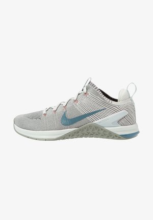 Chaussure de sport Nike Metcon gris clair avec swoosh bleu, dessus tricoté, laçage à l'avant et semelle texturée pour le soutien pendant l'entraînement.