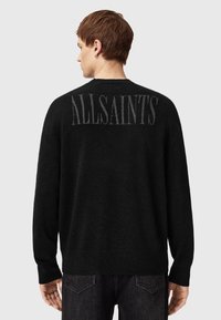 Zwarte gebreide trui met een relaxte pasvorm, voorzien van het "ALLSAINTS" logo in grijs op de rug. Heeft lange mouwen en een ronde halslijn.