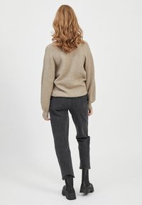 Pull côtelé beige associé à un jean denim noir. La tenue présente une coupe décontractée et est complétée par des bottines noires.
