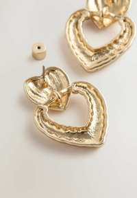 Gold heart-shaped earrings with textured detailing and a layered design. Posts for secure wear included. Finishes are shiny and metallic.