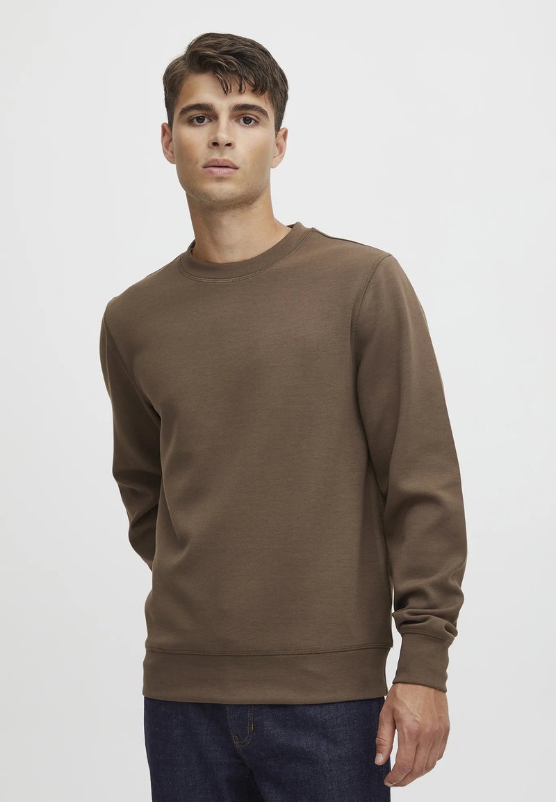 Brun genser laget av mykt stoff, med rund hals, lange ermer og ribbestrikkede mansjetter og nederkant. Enkelt design, ingen grafikk eller mønstre.