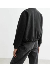 Yli suuri musta fleece-takki, jossa on ribbitunneilla ja helmassa, hienostuneella tekstuurilla ja rentolla istuvuudella, yhdistettynä tummiin farkkuihin.