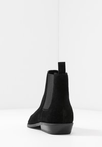 Botas de tobillo de ante negras con una superficie suave, paneles laterales elásticos y un tacón bajo apilado. Diseño minimalista con una lengüeta.