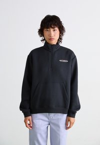 Sweatshirt noir avec demi-zip, col monté et poche avant. Présente le logo "new balance" en blanc, fabriqué en tissu doux.