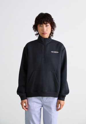 Czarny sweatshirt z pół zamkiem błyskawicznym, wysokim kołnierzem i przednią kieszenią. Posiada logo "new balance" w białym kolorze, wykonany z miękkiego materiału.