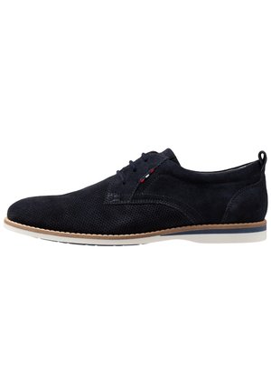 Chaussure de ville à lacets pour homme en daim noir avec texture perforée, bordure beige autour de la semelle, et petit détail de couture rouge, blanc et bleu près des lacets.