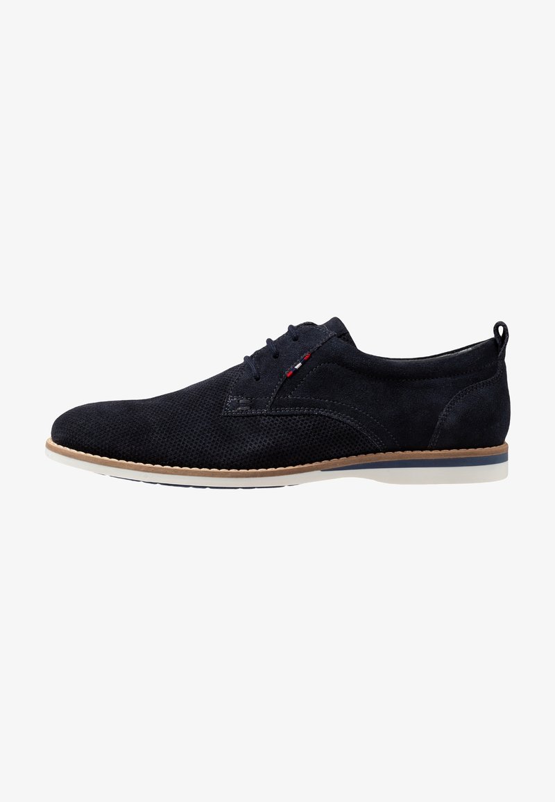 Chaussure de ville à lacets pour homme en daim noir avec texture perforée, bordure beige autour de la semelle, et petit détail de couture rouge, blanc et bleu près des lacets.
