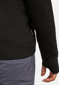 Zwart langhemd met lange mouwen, met een aansluitend ontwerp, een zachte textuur en een zichtbaar merklabel nabij de linker zijnaad. Grijze broek met zakken.