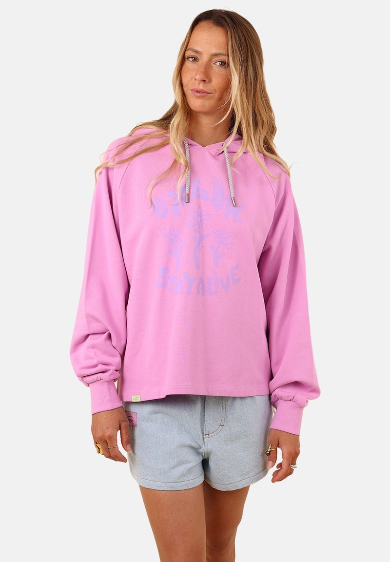 Haut à capuche rose avec une coupe décontractée, doté d'une capuche avec cordon de serrage et d'un texte graphique "STAY ALIVE". Associé à un short en denim clair, mettant en avant un style décontracté.