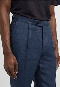 Pantaloni in lino blu scuro con frontale piatto, due bottoni in vita e pieghe visibili, che mettono in mostra una texture liscia.