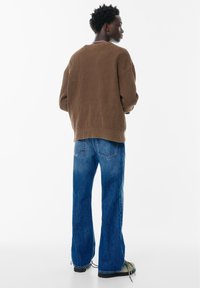 Bruine geribbelde trui, losse pasvorm, ronde halslijn, gecombineerd met blauwe flared jeans met een versleten afwerking en subtiele stikseldetails.