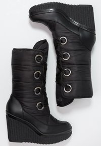 Botas de cuña negras con parte superior de nylon acolchado, ojales de metal y cierre de cordones. Suela de goma texturizada con diseño acanalado.