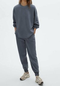 Gray sweatshirt with long sleeves and relaxed fit, paired with matching jogger pants featuring elastic cuffs and side pockets.