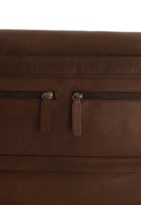 Hnědá kožená taška s texturovaným povrchem, se dvěma kovovými zipy a koženými táhly. Jednoduchý plochý design s jemnými prošitími.