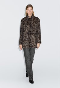 Giacca a fantasia zebratica in morbido tessuto, con colletto, bottoni frontali e due tasche laterali. Abbinata a jeans scuri e scarpe.