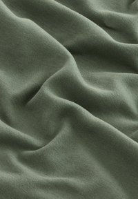 Tissu à texture douce de couleur verte atténuée avec un motif tricoté visible et des plis doux créant des vagues douces.