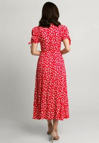 Czerwona sukienka w kwiaty z krótkimi, bufiastymi rękawami, przewężoną talią i zwiewnym dołem. Posiada białe wzory kwiatowe i sznurki przy rękawach.