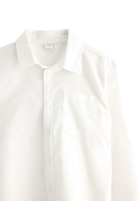 Biała koszula z długim rękawem, z kołnierzykiem z ostrym wyłożeniem, jedną kieszenią na piersi oraz sześcioma guzikami na przodzie. Materiał wydaje się gładki.