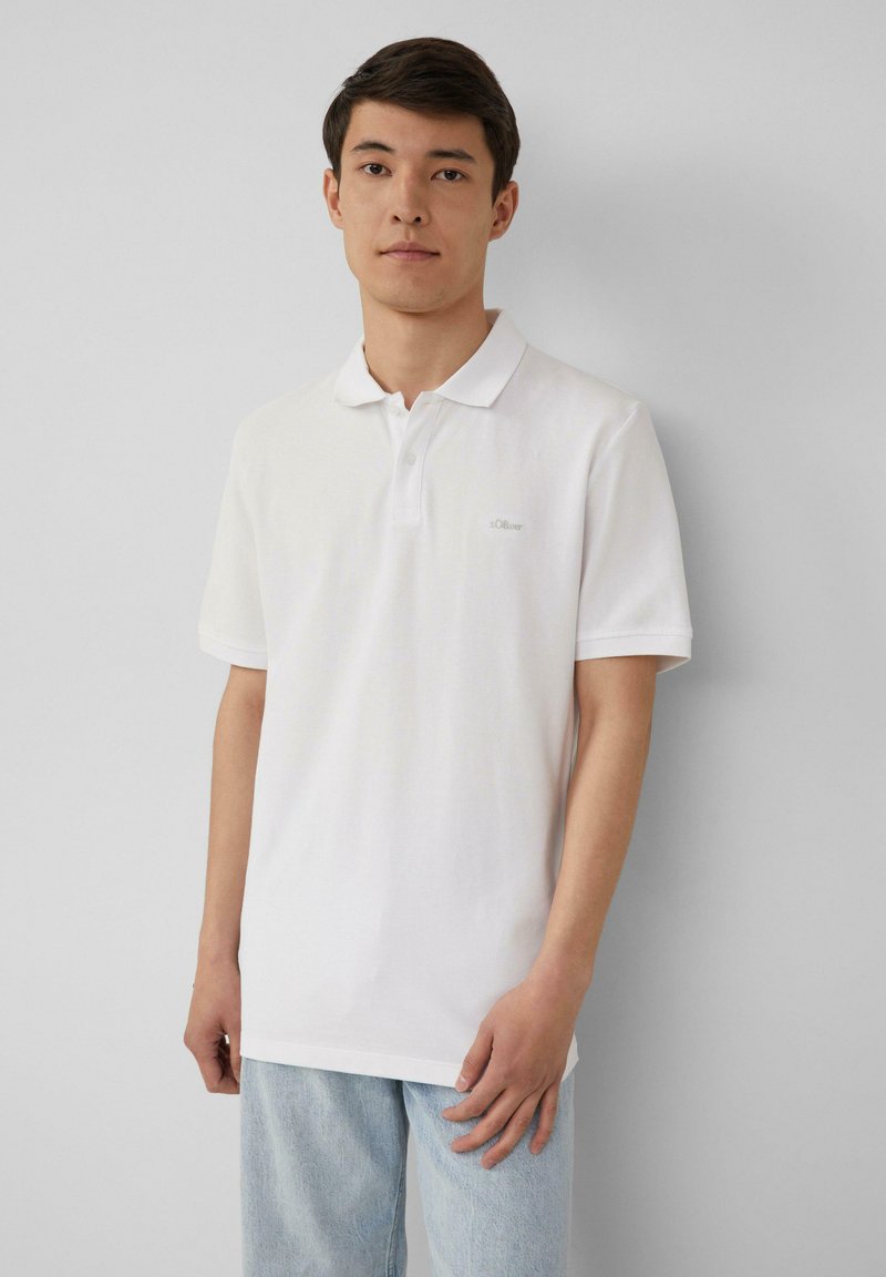 Witte polo shirt van katoen, met een klassieke kraag, korte mouwen en een klein logo op de linkerkant van de borst. Gecombineerd met lichtblauwe jeans.