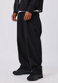 Pantalons noirs amples en matière légère, associés à des chaussures de sport noires avec amorti à air visible.