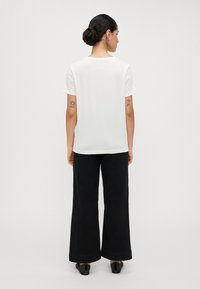 White short-sleeved t-shirt with a relaxed fit, paired with wide black trousers, displayed from the back, featuring visible tattoos on arms.