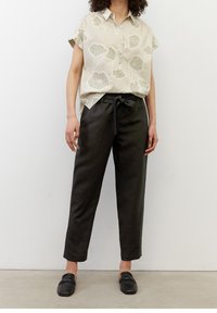 Lichtbeige shirt met korte mouwen met bladerenprint, gecombineerd met zwarte hoge taille broek met strik taille. Zwarte instappers.