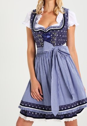 Kvinde iført en blå og hvid traditionel dirndl-kjole med blomsterprint, snørede liv, puffede ærmer og en stor ternet sløjfe i taljen.