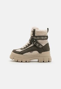 Kraftige ankelstøvler i olivengrøn med cremefarvet faux shearling, der har en tyk platformssål og et mærket bånd på tværs af forsiden.