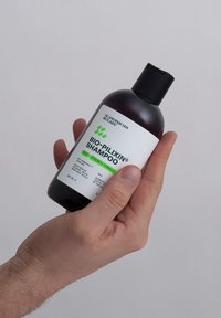 Bouteille en verre foncé de shampooing BIO-PILIXIN avec un capuchon noir, présentant une étiquette blanche avec du texte vert, tenue dans une main. Taille de 250 ml.
