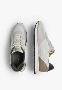 Zapatillas gris claro con una combinación de partes de ante y malla, suela blanca, parte inferior negra y ligeros acentos naranjas cerca de los cordones.