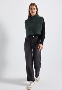 Groen gestructureerd cropped sweater over een zwart langemouwenshirt, gecombineerd met hooggesneden donkere jeans en witte sneakers.