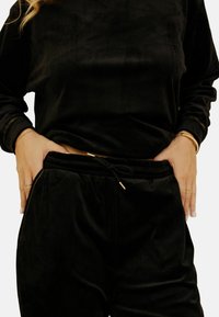 Ensemble de loungewear en velours noir avec une coupe décontractée. Comprend un haut à manches longues et un pantalon à cordon, rehaussé de détails en métal doré.