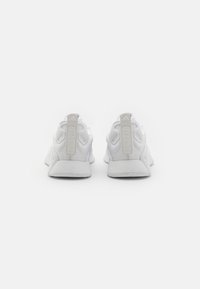 Chaussures de sport blanches avec un design en maille, un talon renforcé et une semelle texturée. Présente une étiquette grise "TRAINING" sur le talon pour le détail.