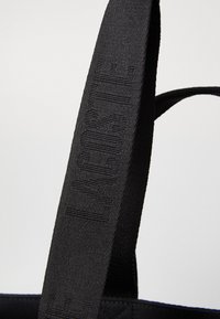Cinghia di una borsa in tessuto nero con il nome del marchio "HUGO" impresso in una texture in rilievo lungo tutta la sua lunghezza.