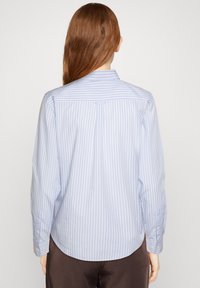 Light blue and white striped shirt with a button-down collar, long sleeves, and curved hem; made of smooth, lightweight fabric.