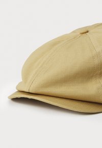 Licht kaki pet gemaakt van gestructureerde stof met een ronde kroon, een korte, gebogen klep en zichtbare naden die het gestructureerde ontwerp accentueren.