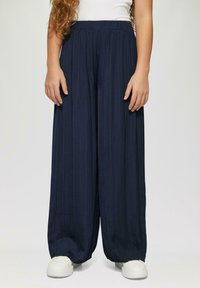 Granatowe spodnie o szerokich nogawkach z fakturowanym, plisowanym wzorem oraz elastycznym pasem, połączone z białymi sneakersami.