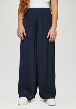 Marineblaue weite Hosen mit einem strukturierten, gefältelten Design und einem elastischen Bund, kombiniert mit weißen Sneakers.