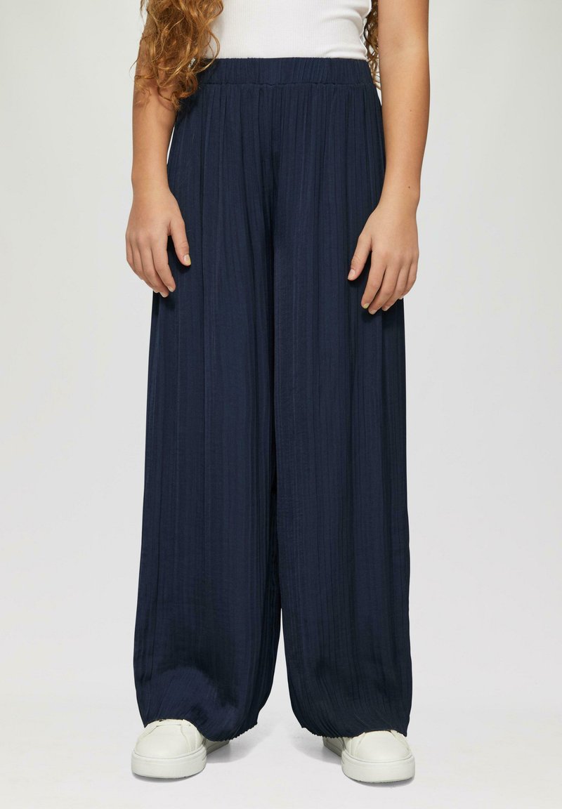 Granatowe spodnie o szerokich nogawkach z fakturowanym, plisowanym wzorem oraz elastycznym pasem, połączone z białymi sneakersami.