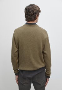 Olijfgroen wollen sweater met een geribde ronde hals en mouwen. De achterkant is iets losvallend met een zachte textuur en minimale naden.
