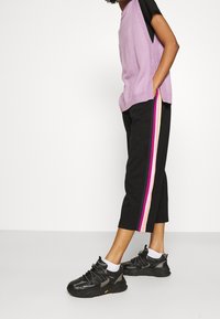 Top a maglia lilla con aperture laterali, abbinato a pantaloni neri alla caviglia con strisce laterali multicolori. Sneakers nere con tomaia texture.