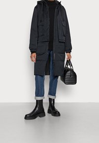 Czarna kurtka puchowa z kapturem, dwie przednie kieszenie, noszona na czarnym topie. Jasnoniebieskie dżinsy ze zwiniętymi mankietami, czarne buty Chelsea i czarna torebka.