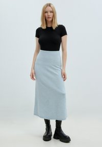 Zwarte geribbelde top met korte mouwen, gecombineerd met een lichtblauwe hoge maxi rok. Het model draagt stevige zwarte platformlaarzen. Glad textuur.
