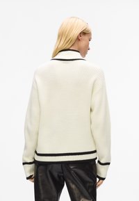 Pull en tricot côtelé blanc avec une bande d'accent noir au col et à l'ourlet. Présente des manches longues et une coupe décontractée.