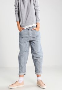 Ljusgrå sweatshirt med spetsdetaljer, tillsammans med lösa, randiga denimbyxor med uppvikt fåll och en sliten del. Beiga sneakers.