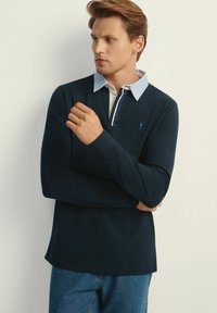Granatowa polo z długim rękawem, z kontrastującym jasnoniebieskim kołnierzykiem i plisą, z małym logo na piersi oraz luźnym krojem.