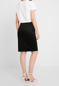 Svart pennkjol med slät textur, knälång och med slits bak. Matchas med en vit t-shirt och beige högklackade sandaler.