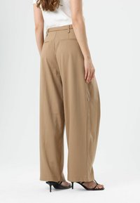 Beige wide-leg trousers with a smooth texture, featuring a high waist, belt loops, and back pockets, worn with black heeled sandals.